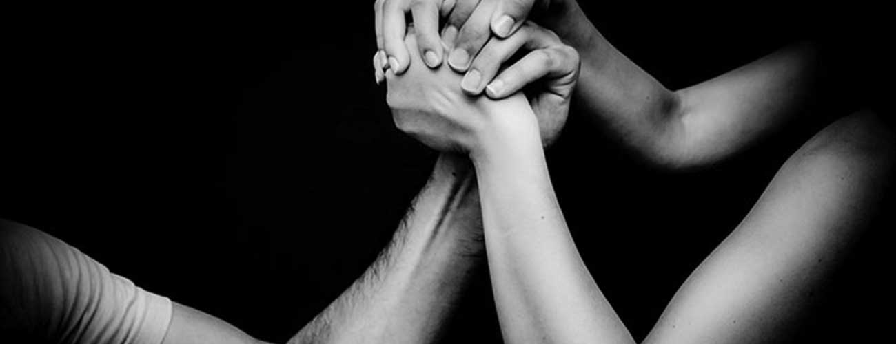 Photograph of a pair of hands clasped around another hand, against black background (Creative Commons)