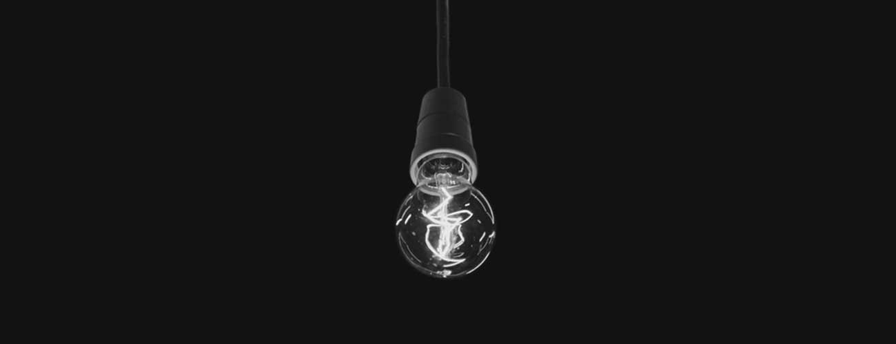 Photograph of lightbulb hanging against a black background, by Tom Mrazek