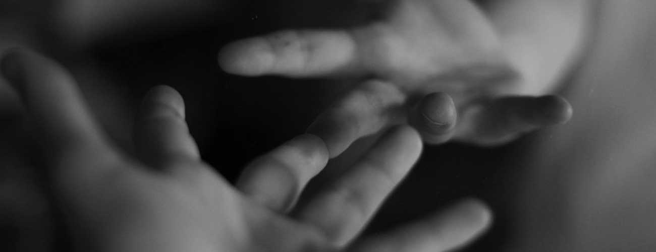 Photograph of hands reaching towards each other, fingertips touching, by Emsiproduction